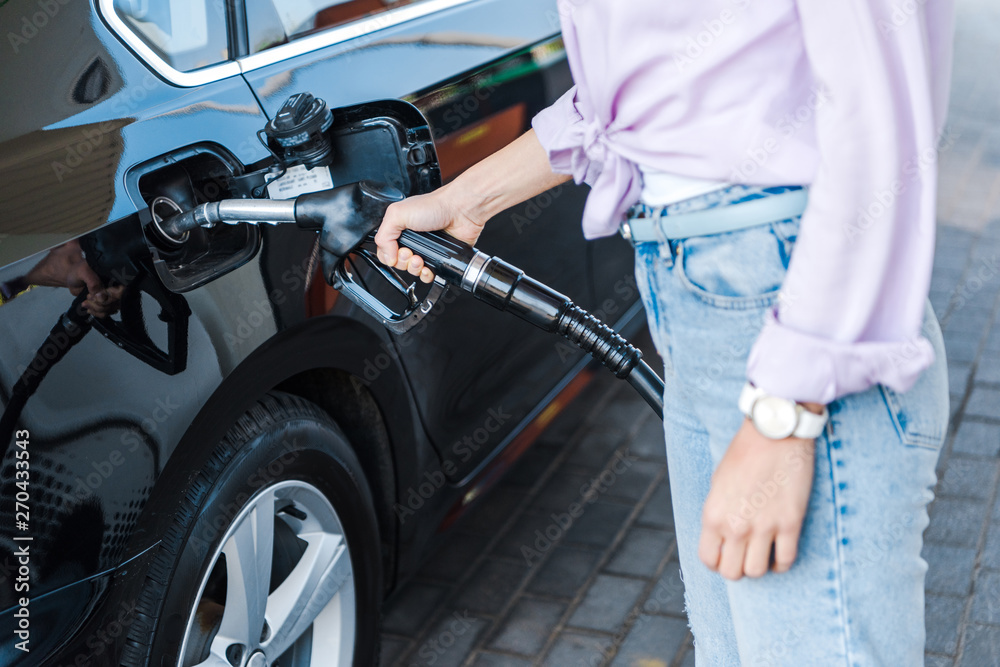 cropped view of woman holding fuel pump while refueling black car with benzine