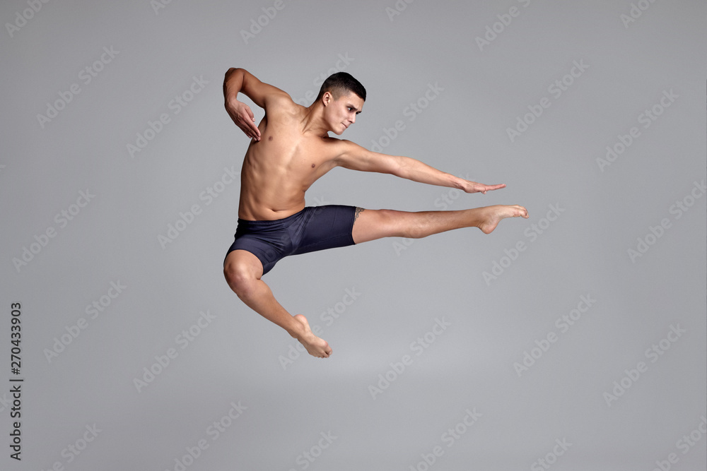 Photo of a handsome man ballet dancer, dressed in a black shorts, making a dance element against a gray background in studio. Photo of a handsome man ballet dancer, dressed in a black shorts, making a dance element against a gray background in studio.