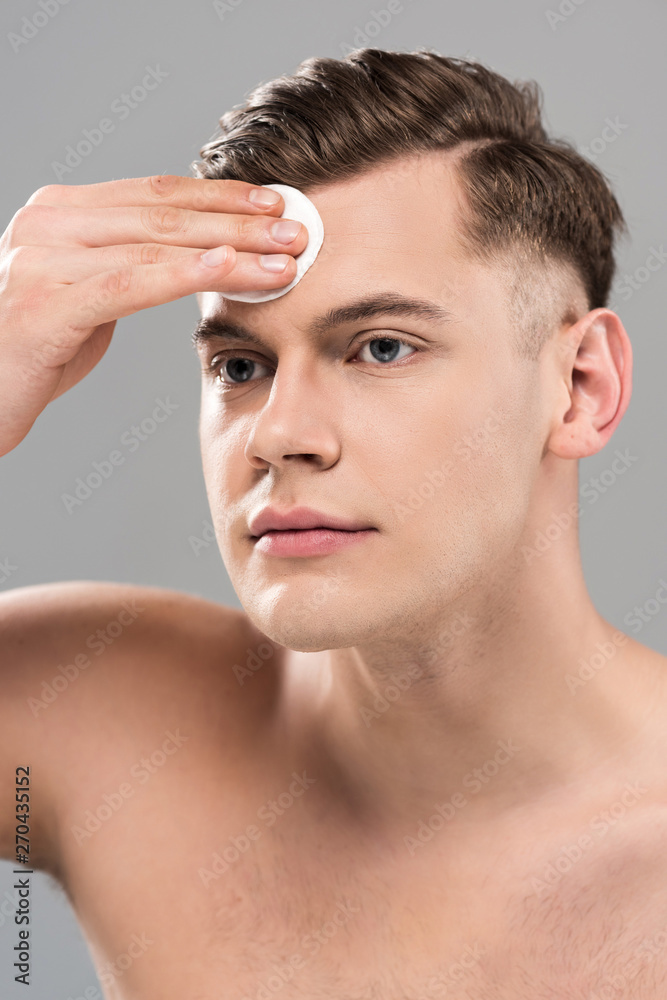 Obraz premium handsome young man wiping face with cotton pad isolated on grey