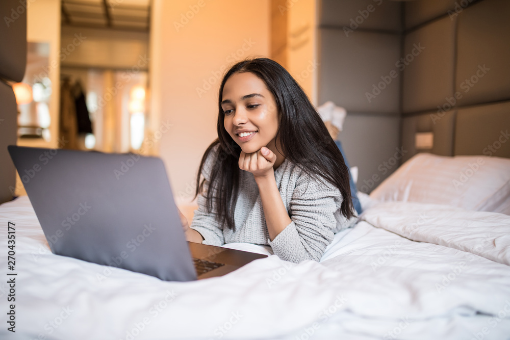 Young happy woman with laptop lying on bed at home. Lazy morning Young happy woman with laptop lying on bed at home. Lazy morning