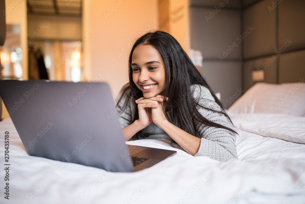 Young happy woman with laptop lying on bed at home. Lazy morning Young happy woman with laptop lying on bed at home. Lazy morning
