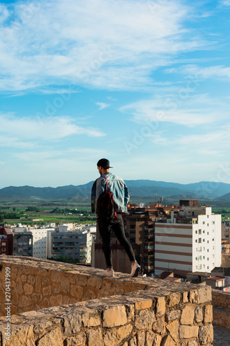 Back view of young man looking at city from castle rooftop