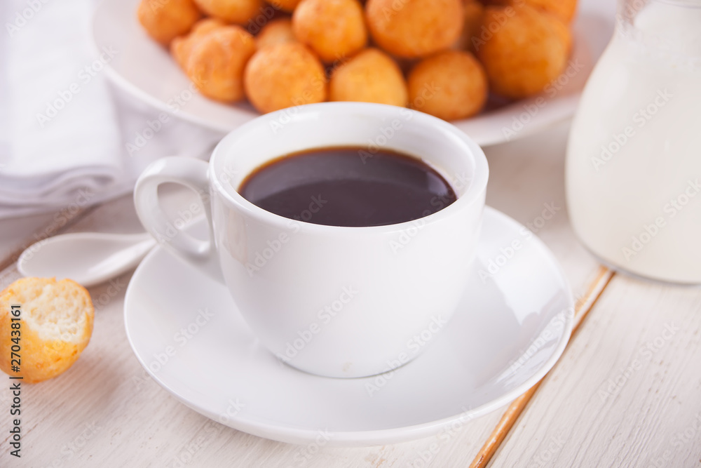 Cup of coffee with small balls of freshly baked homemade cottage cheese doughnuts in a plate on a background. Cup of coffee with small balls of freshly baked homemade cottage cheese doughnuts in a plate on a background.