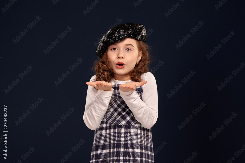 Stylish brunette kid is posing in studio on a black background. Children's fashion.