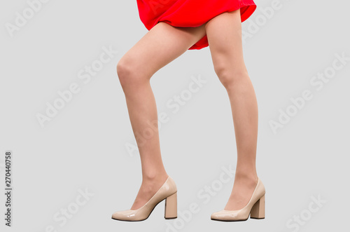 Beautiful legs of a girl in a red dress in shoes standing on the floor