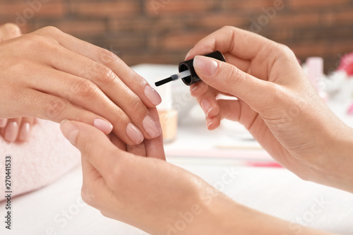 Manicurist applying polish on client's nails at table, closeup. Spa treatment photo