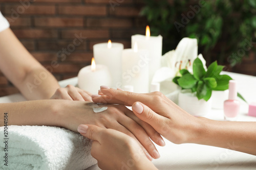 Cosmetologist applying cream on woman's hand at table in spa salon, closeup with space for text
