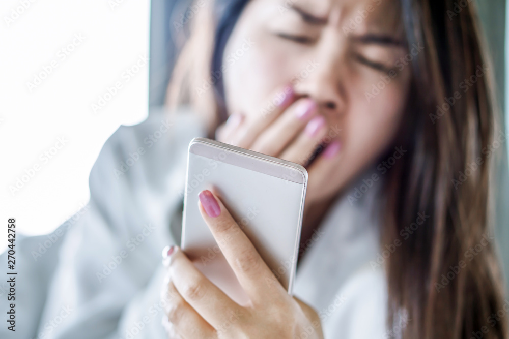 Asian woman yawning on bed hand holding smart phone feeling tired and sleepy ,social addict concept Asian woman yawning on bed hand holding smart phone feeling tired and sleepy ,social addict concept