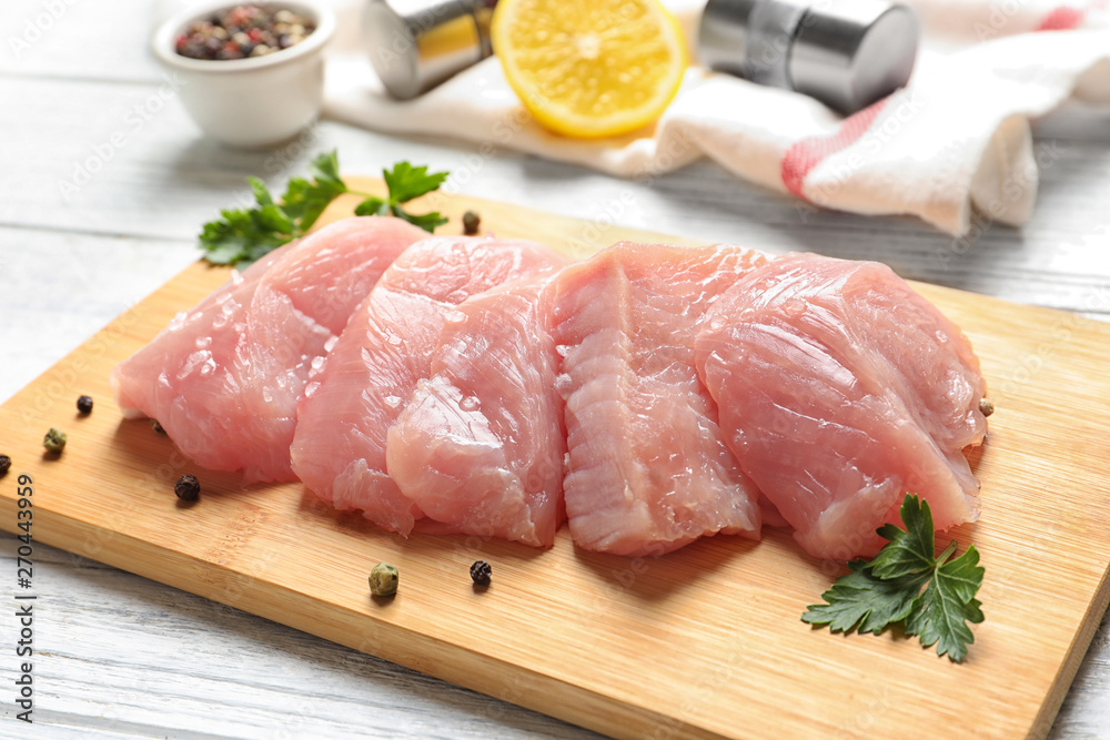 Board with cut raw turkey fillet and parsley on wooden table Board with cut raw turkey fillet and parsley on wooden table