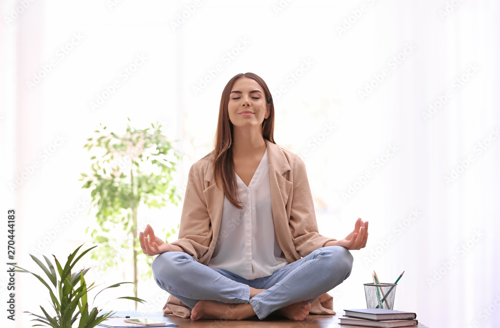 Young businesswoman meditating at workplace. Zen concept - obrazy, fototapety, plakaty 