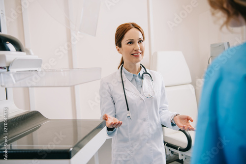selective focus of beautiful smiling doctor in white coat welcoming patient in hospital