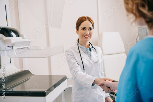 selective focus of smiling radiologist shaking hands with patient in hospital
