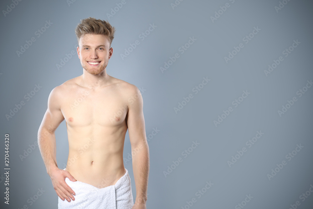 Fototapeta premium Portrait of young man with slim body in towel on grey background. Space for text