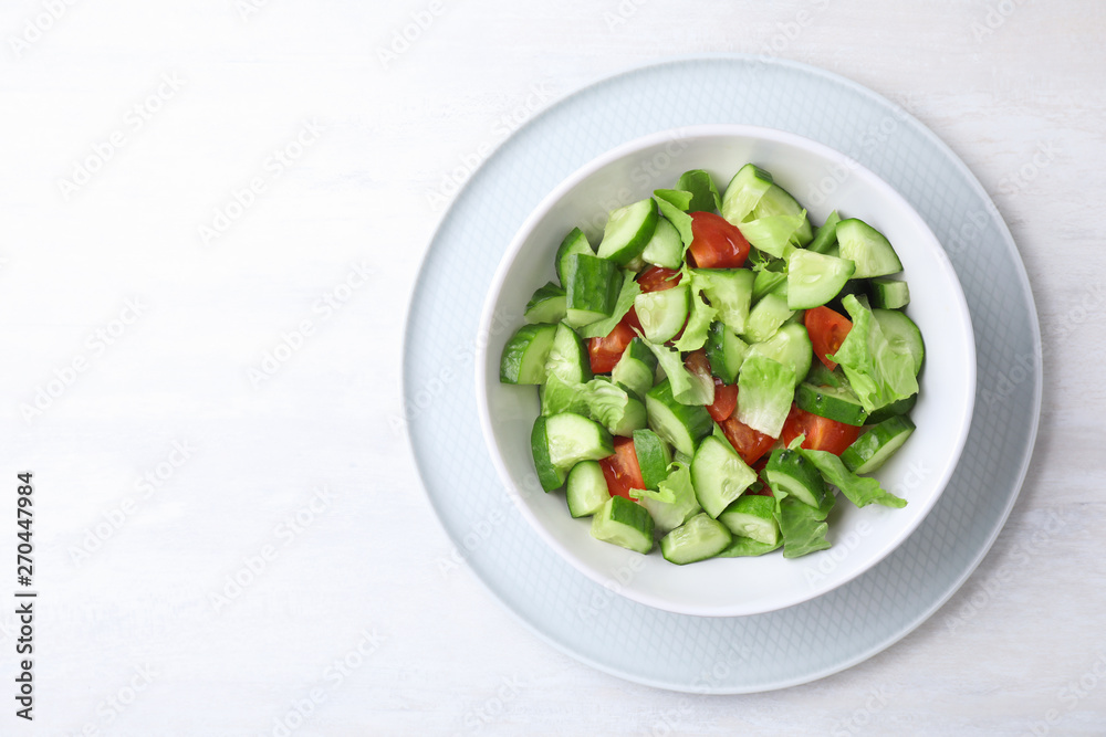 Bowl of vegetarian salad with cucumber, tomato and lettuce on light background, top view. Space for text Bowl of vegetarian salad with cucumber, tomato and lettuce on light background, top view. Space for text