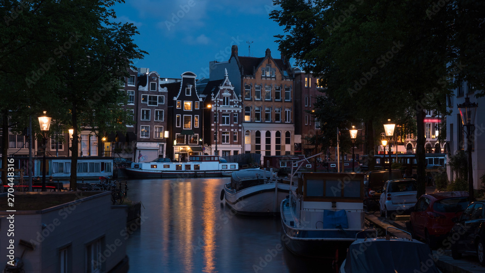 Amsterdam night scene with traditional houses, boats moored along the canal and lit lanterns, Netherlands