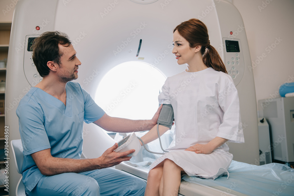 Obraz premium handsome doctor measuring patients blood pressure with tonometer while sitting at mri scanner