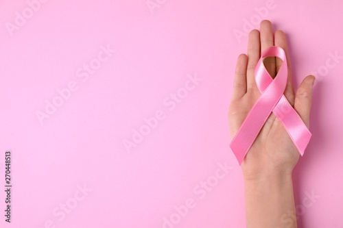 Woman with symbolic ribbon of breast cancer awareness and space for text on color background, top view. Gynecological care