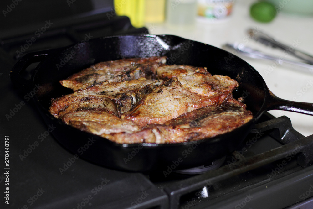 Country style cut pork ribs in a cast iron pan on the stove top. Country style cut pork ribs in a cast iron pan on the stove top.