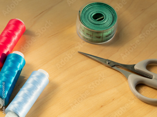 Colored sewing thread, measuring green tape and scissors on the table.