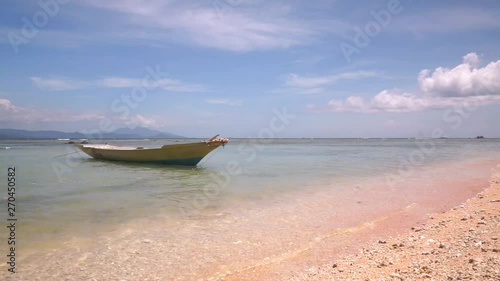 Small wooden boat bobs and swings on calm waves on leash at picturesque deserted beach without people. Calm sea waves of the turquoise Indian Ocean washes the sandy shore. 50 frames per second Full HD photo