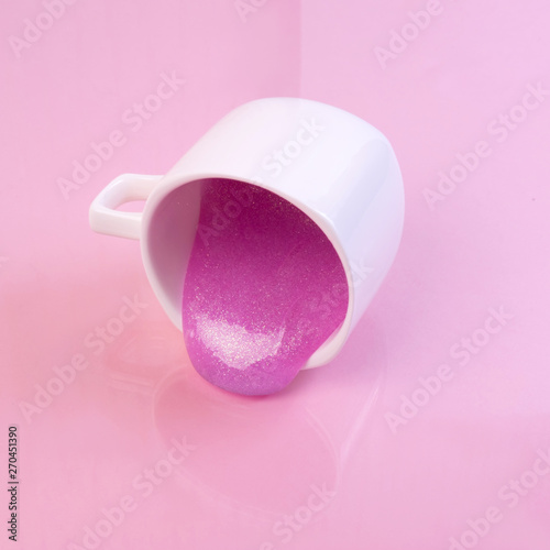 Bright pink glitter slime comes out of mug. White cup on pink background. Art neon surrealism and minimalism concept photo