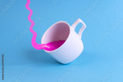 Bright pink glitter slime comes in mug. White cup on blue background. Art neon surrealism and minimalism concept photo