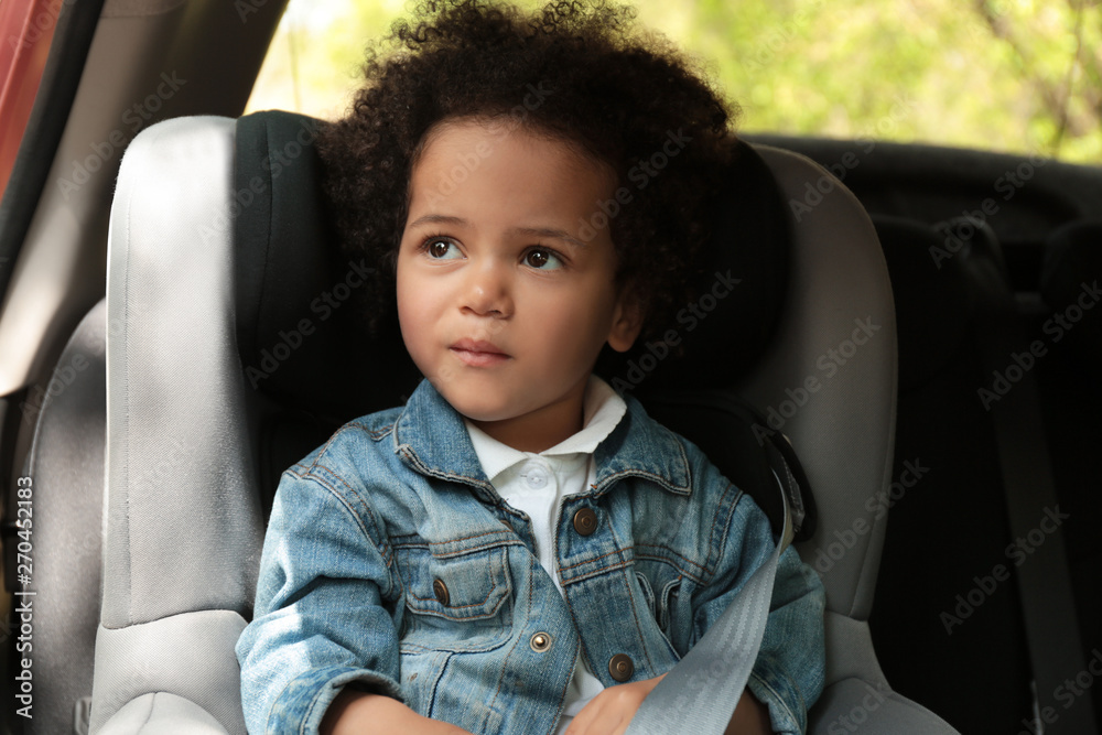 Cute African-American child sitting in safety seat inside car. Danger prevention