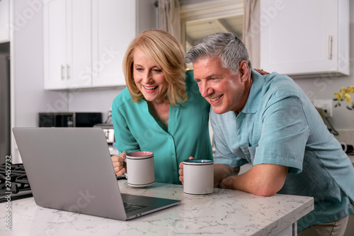 Happy senior couple retired at home enjoying the internet together, smiling laughing and cheerful.