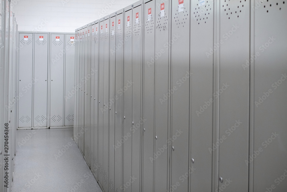 A row of steel grey lockers along the white wall. Dressing room at the enterprise or in the gym. Narrow corridor