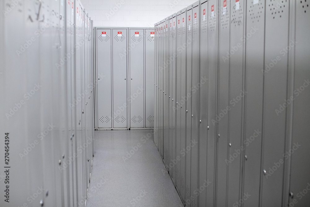 A row of steel grey lockers along the white wall. Dressing room at the enterprise or in the gym. Narrow corridor