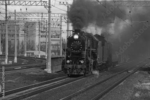 Black and white retro steam train in clouds of smoke rides by rail, rolling tourists