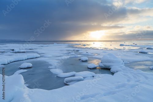 Sunset with snowy boulders and beach landscape. Baltic sea, winter time.