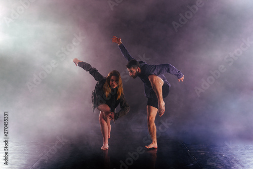 Two modern dancers stretching their shoeless feet high in the air surrounded by smoke on stage.