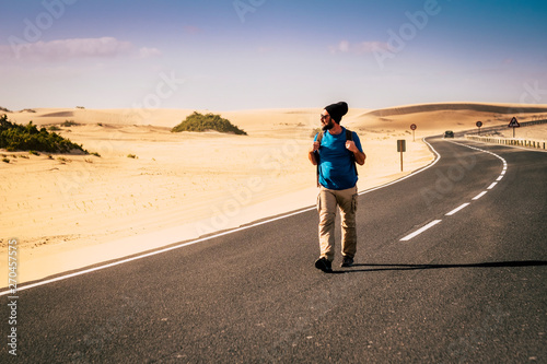 Lonely adventure traveler walk in the middle of the long scenic road with backpack - wanderlust travel lifestyle for adult people - desert and asphalt beautiful place for alternative vacation