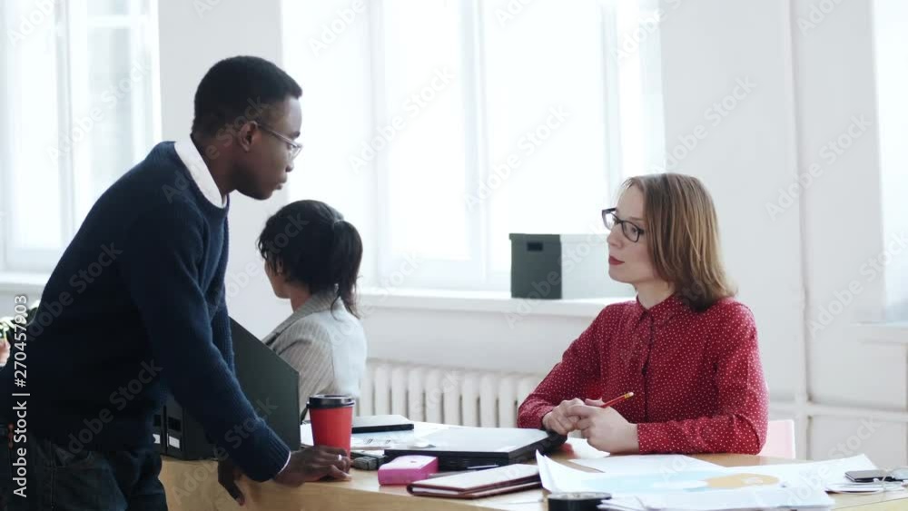 Young African office worker man talking to beautiful middle aged Caucasian boss woman at healthy mutiethnic workplace. Young African office worker man talking to beautiful middle aged Caucasian boss woman at healthy mutiethnic workplace.