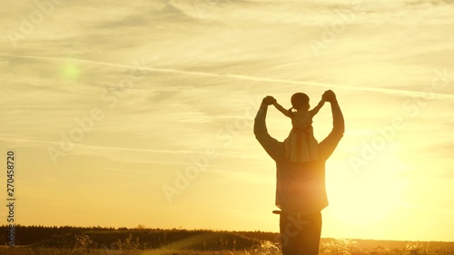 Dad dancing on his shoulders with his daughter in sun. Father travels with baby on his shoulders in rays of sunset. child with parents walks at sunset. happy family resting in park. family concept