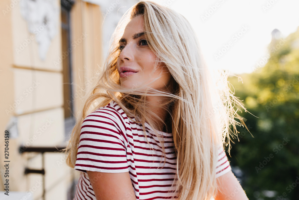 Ecstatic blonde girl with  happy face expression looking up and dreaming about something. Close-up portrait of elegant young woman in trendy t-shirt spending time at balcony.