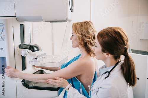 young radiographer standing near patient while making mammography test on x-ray machine photo