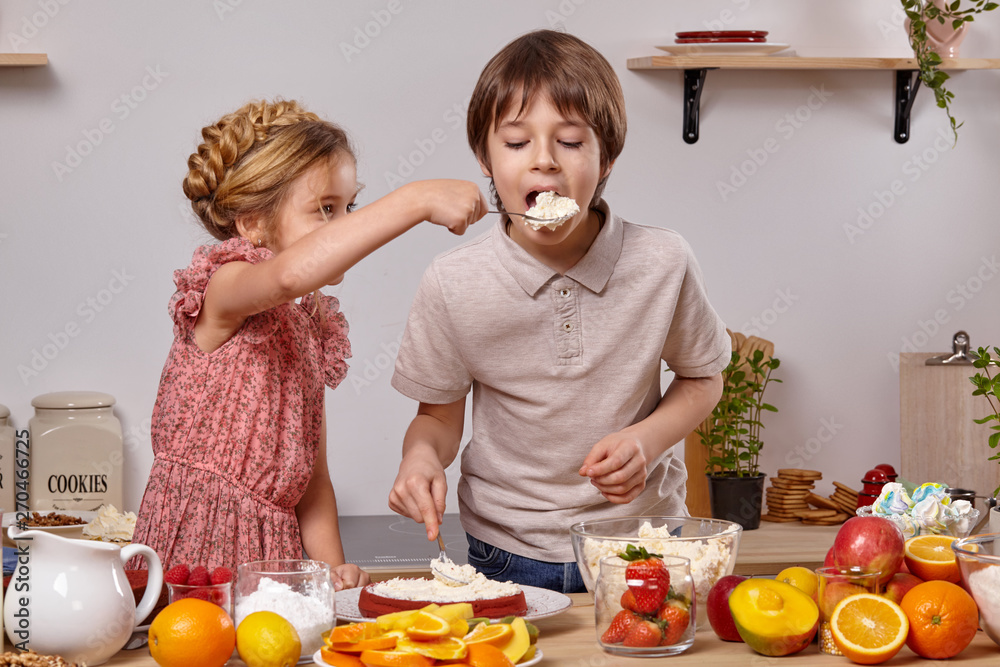 Little friends are making a cake together at a kitchen against a white wall with shelves on it. Little friends are making a cake together at a kitchen against a white wall with shelves on it.