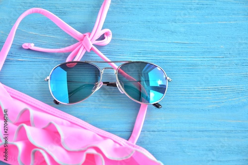 Aviator sunglasses with trendy pink swimsuit on blue wooden background. Selective focus. Summer concept with pink neon bikini and colorful eyeglasses on textured blue backdrop. Hello summer 