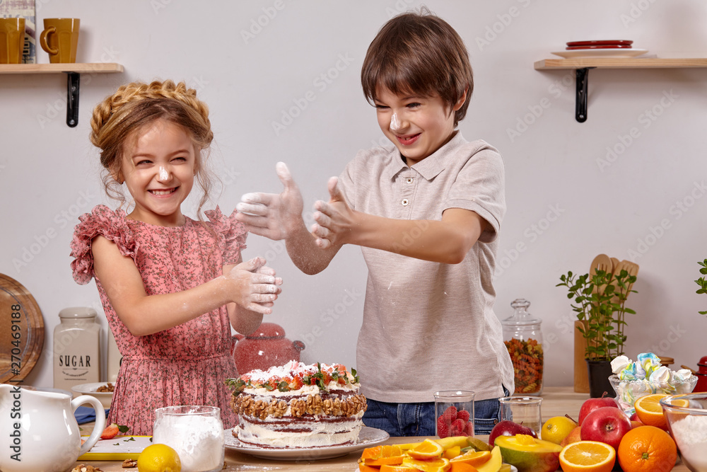 Little friends are making a cake together at a kitchen against a white wall with shelves on it. Little friends are making a cake together at a kitchen against a white wall with shelves on it.