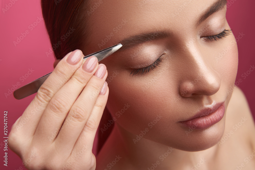 Beautician with elegant manicure plucking young lady eyebrows with tweezers