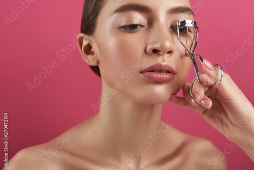 Beautician correcting lady eyelashes with curling tongs photo