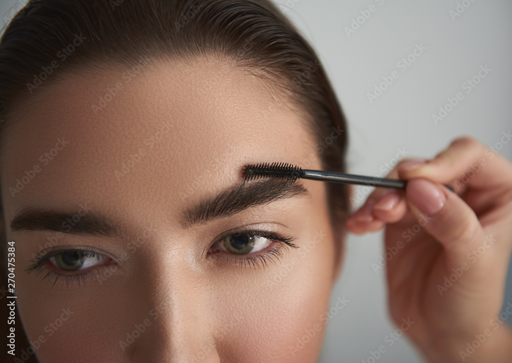 Woman is having brows styled against grey background