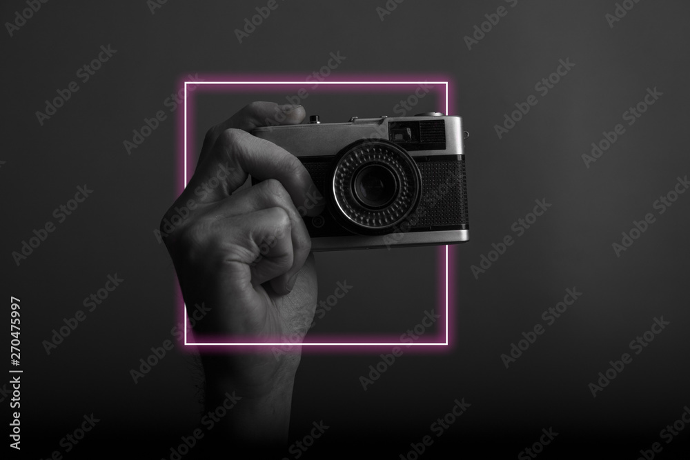 Male hand holding a vintage film camera with abstract neon light glow