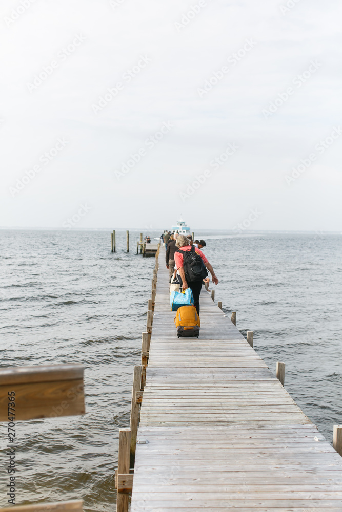 People Pulling Suitcases Along Boardwalk To A Ferry