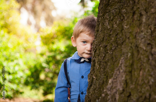 Cute little boy leaning against big tree and shy in summer, child portrait outdoors photo