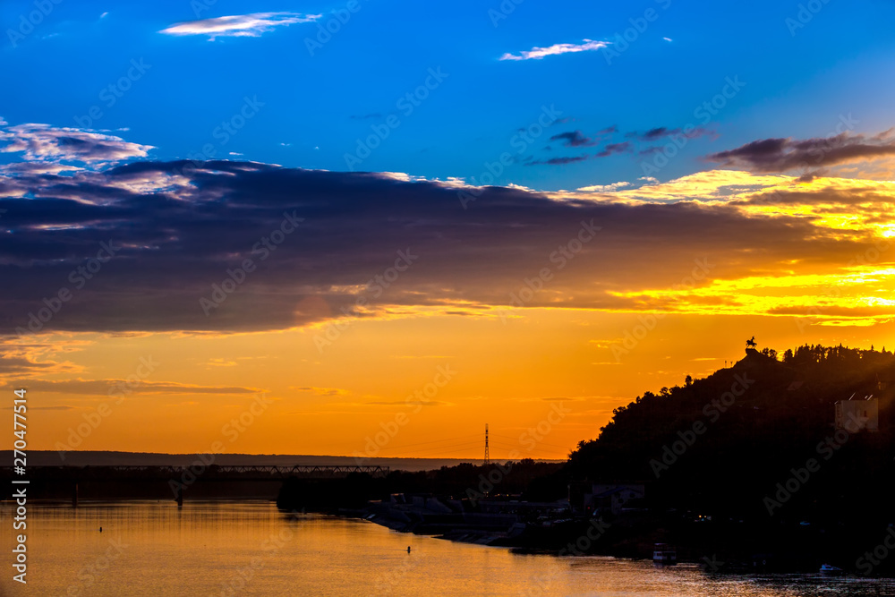 Silhouette of monument to Salawat Yulaev against a bright yellow blue sky with clouds and orange sun disk at city sunset on the river bank. Salavat Yulayev, Ufa, Bashkortostan, Russia. Silhouette of monument to Salawat Yulaev against a bright yellow blue sky with clouds and orange sun disk at city sunset on the river bank. Salavat Yulayev, Ufa, Bashkortostan, Russia.