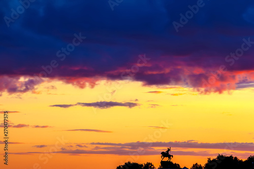 Silhouette of monument to Salawat Yulaev, folk hero on a horse against a bright yellow purple violet sky with clouds and orange sun disk at city sunset. Salavat Yulayev, Ufa, Bashkortostan, Russia.