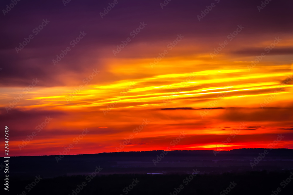 The fiery sky above the silhouette of the horizon of the Russian steppe, bright colorful clouds of red yellow color hide the setting sun. Sunset over Ufa, Bashkortostan, Russia.